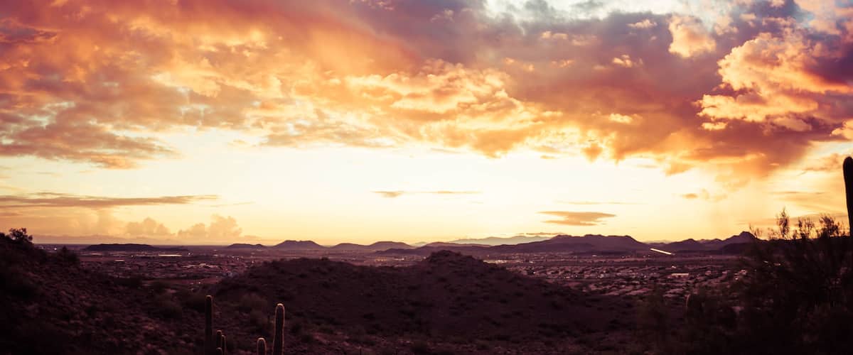 A panorama of a dramatic sunset over the desert with saguaro cactus and colorful clouds in the sky.