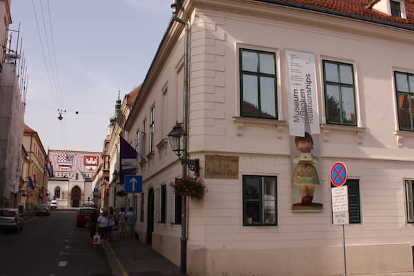 Uma rua com edifícios, uma placa indicando Museum der Broking Relishships e uma placa de proibido estacionar.