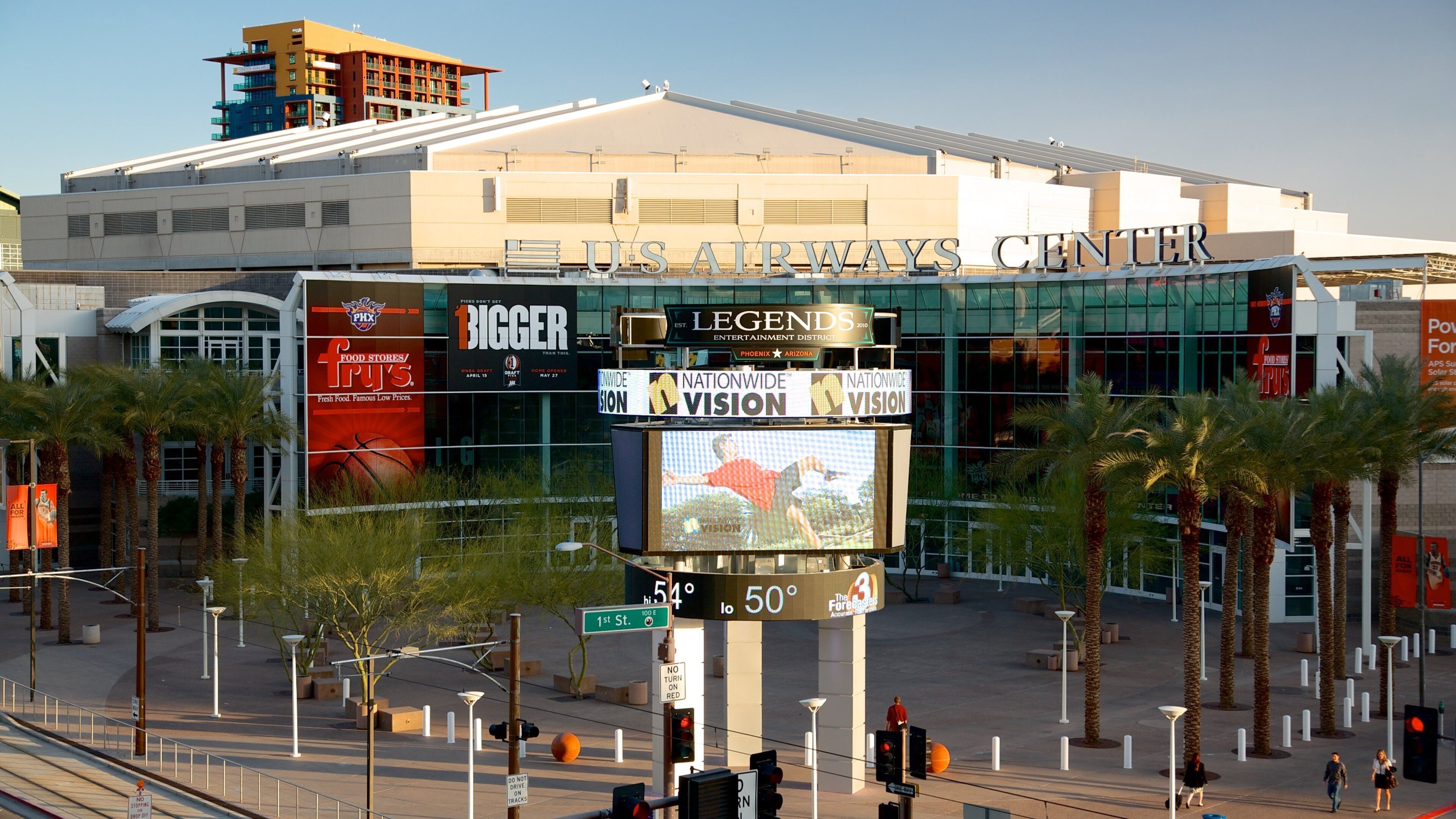 A large indoor arena with a digital scoreboard, palm trees, and various advertisements.