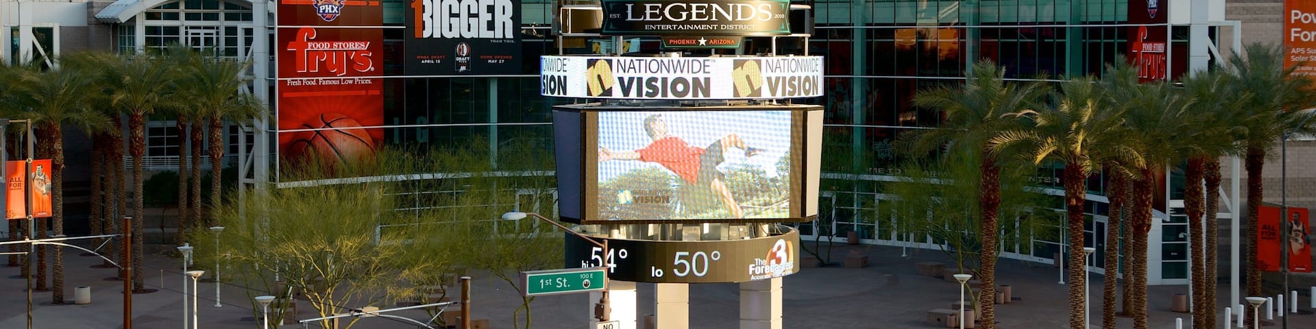 A large indoor arena with a digital scoreboard, palm trees, and various advertisements.
