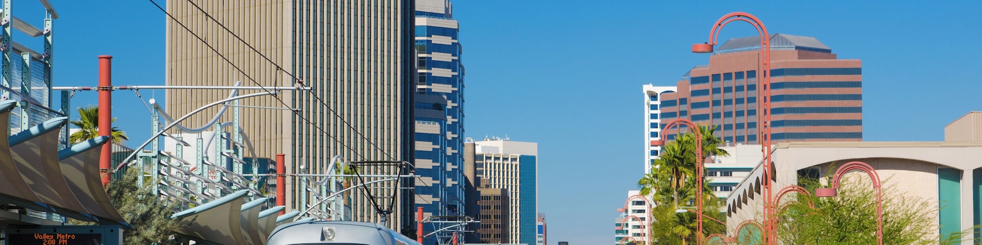 Eine moderne Stadtstraße mit einer Straßenbahn, hohen Gebäuden und blauem Himmel.