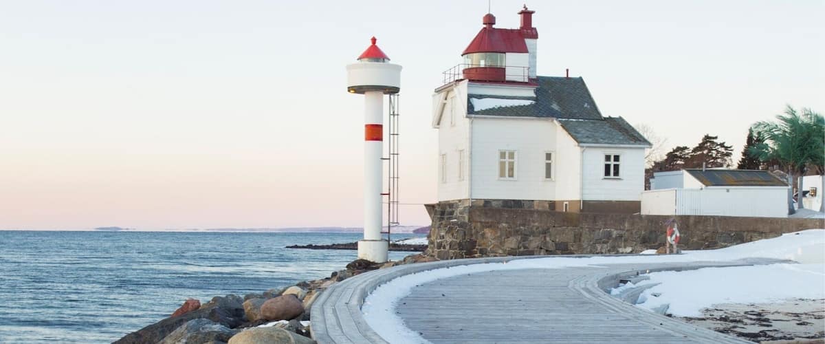 A lighthouse and a white building by the sea with a wooden walkway.