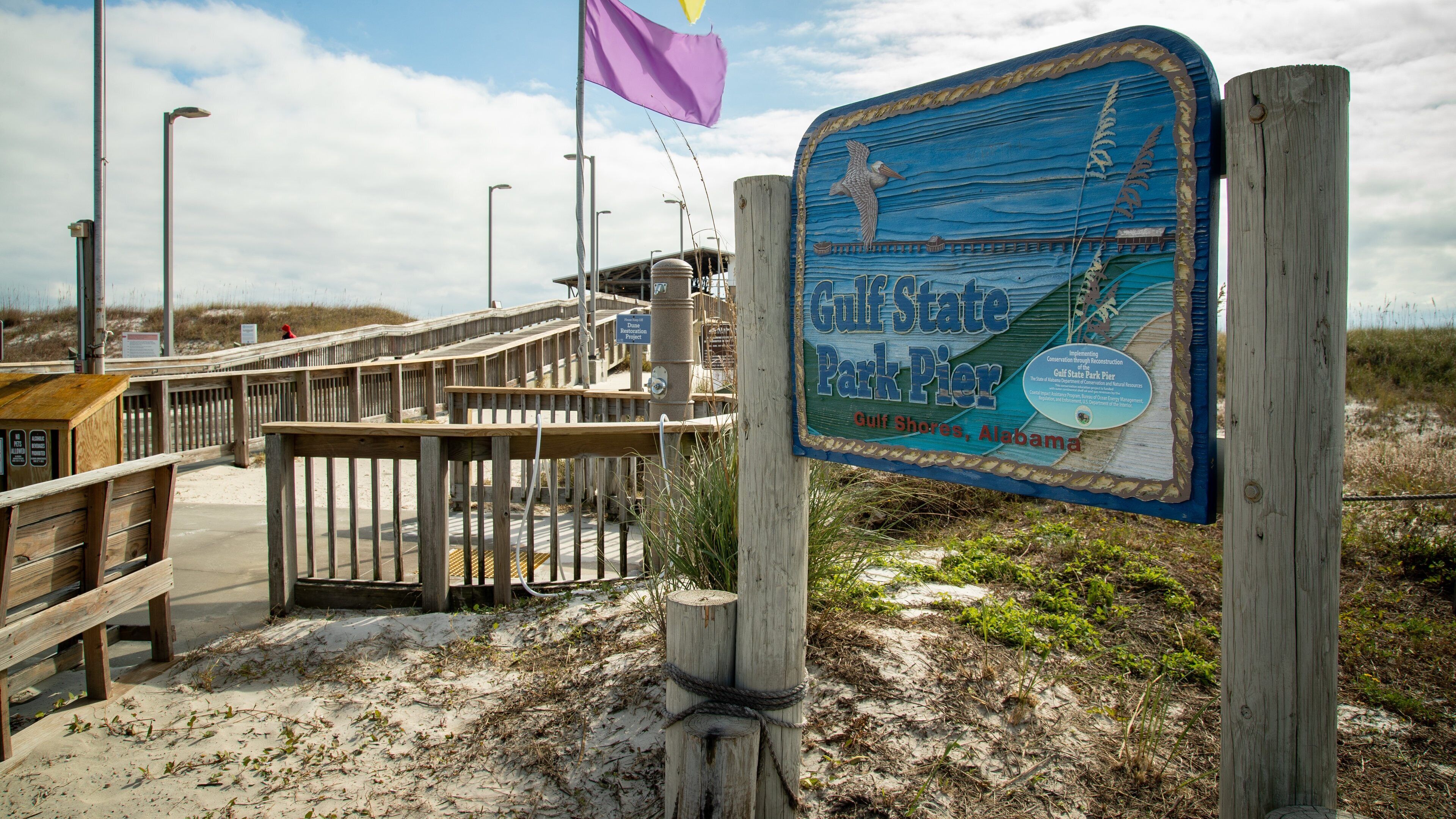 A wooden boardwalk leading to Gulf State Park Pier with a signboard.