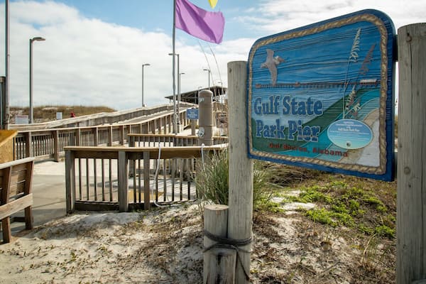 En træbro, der fører til molen ved Gulf State Park, med et skilt.