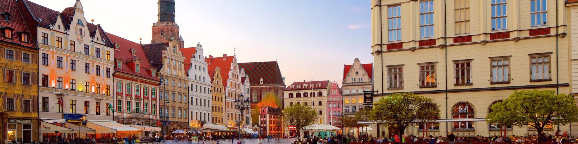 A historic European square with cobblestone pavement, traditional buildings, and a prominent tower.