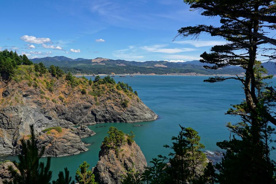 A coastal landscape with rocky cliffs, dense forests, and a calm sea.