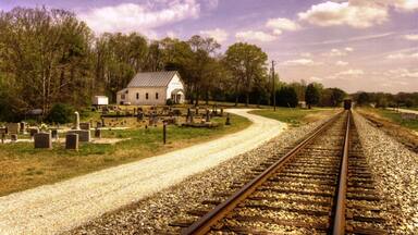 A rural landscape with a gravel road, a white building, and a cemetery.