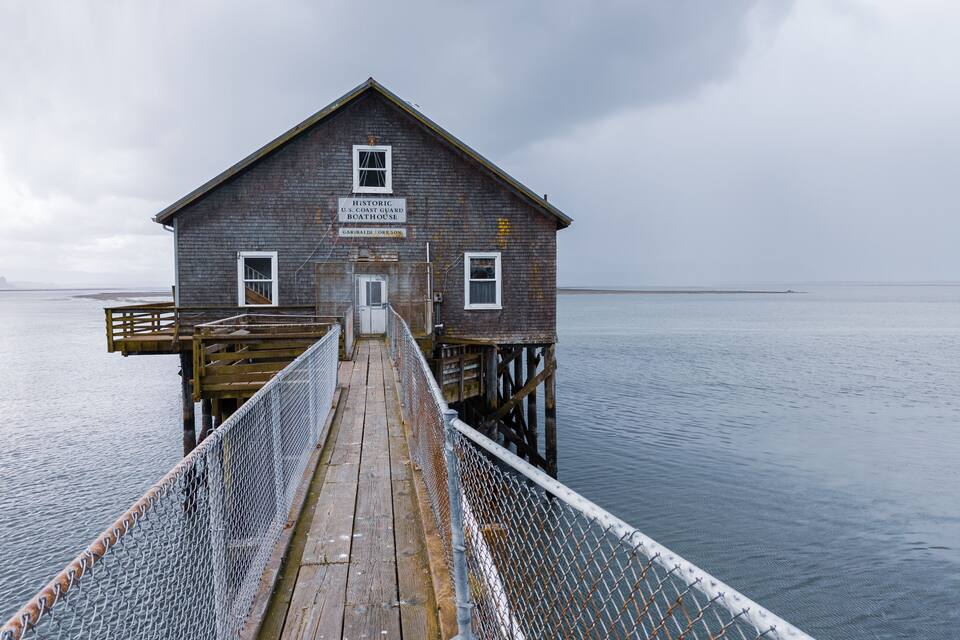 A historic U.S. Coast Guard boathouse in Garibaldi, Oregon, with a wooden pier leading to it.
