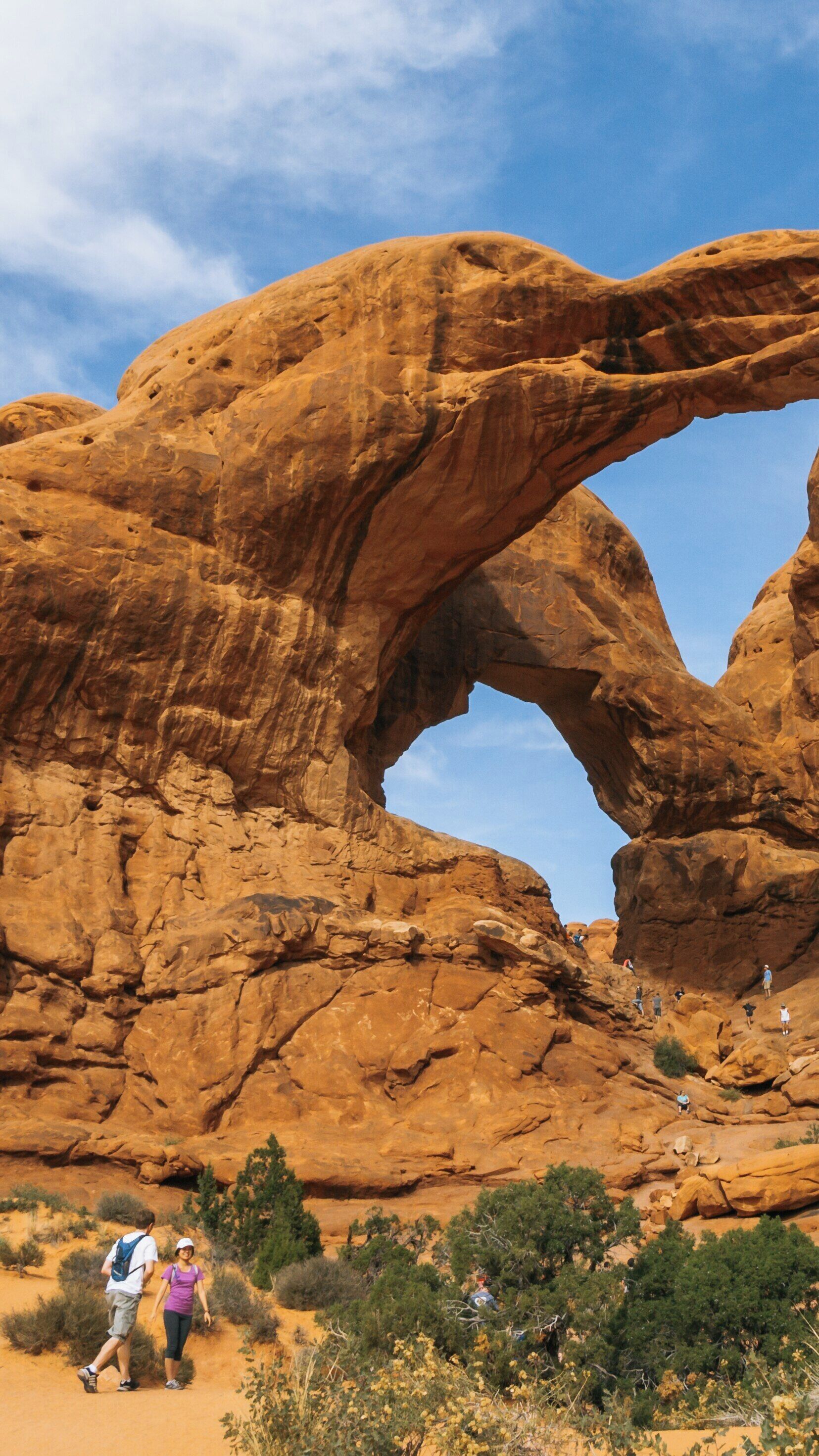Double Arch in Moab, Utah draws hikers and nature enthusiasts under its towering formations during a sunny day