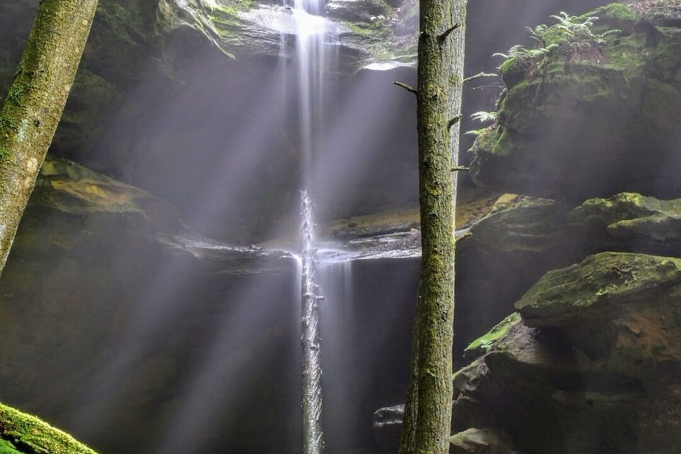 A waterfall in a forested area with sunlight filtering through the trees.