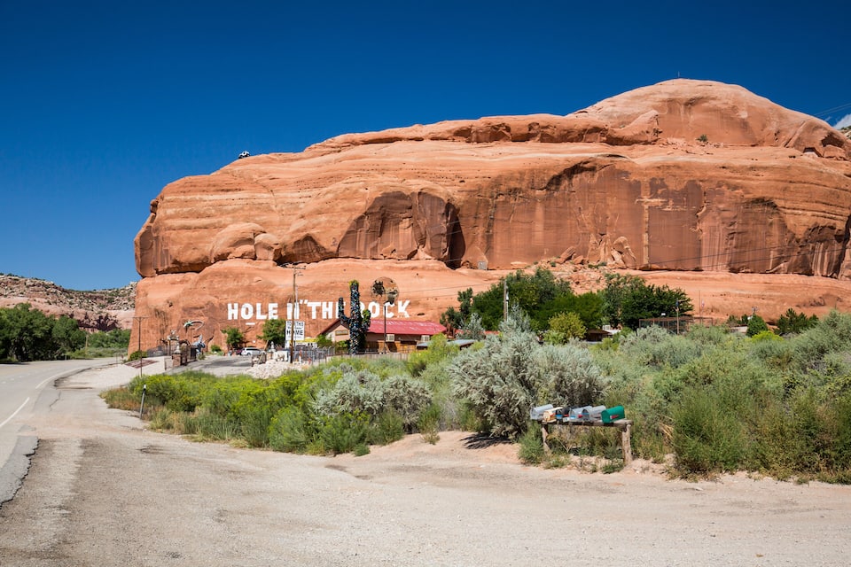A large red rock formation with the text "HOLE IN THE ROCK" and a small building at its base.