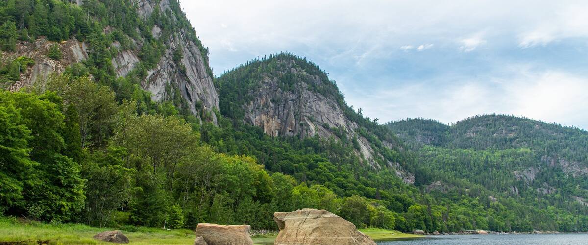 A river with large boulders in a forested valley with mountains in the background.