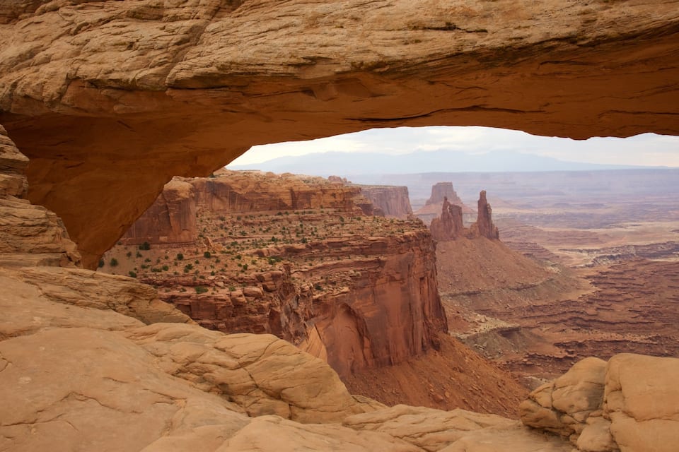 A rock arch formation with a view of a desert landscape and distant mountains.