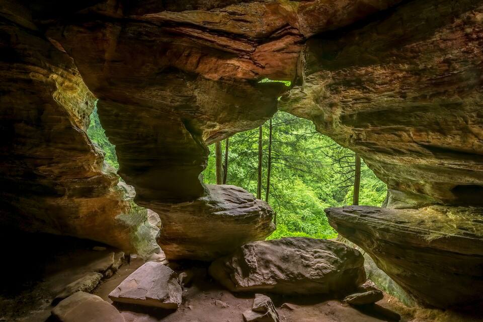 A cave with large rock formations and a view of a forest.