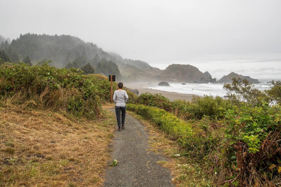 A person walking on a coastal path with a view of the ocean and hills.
