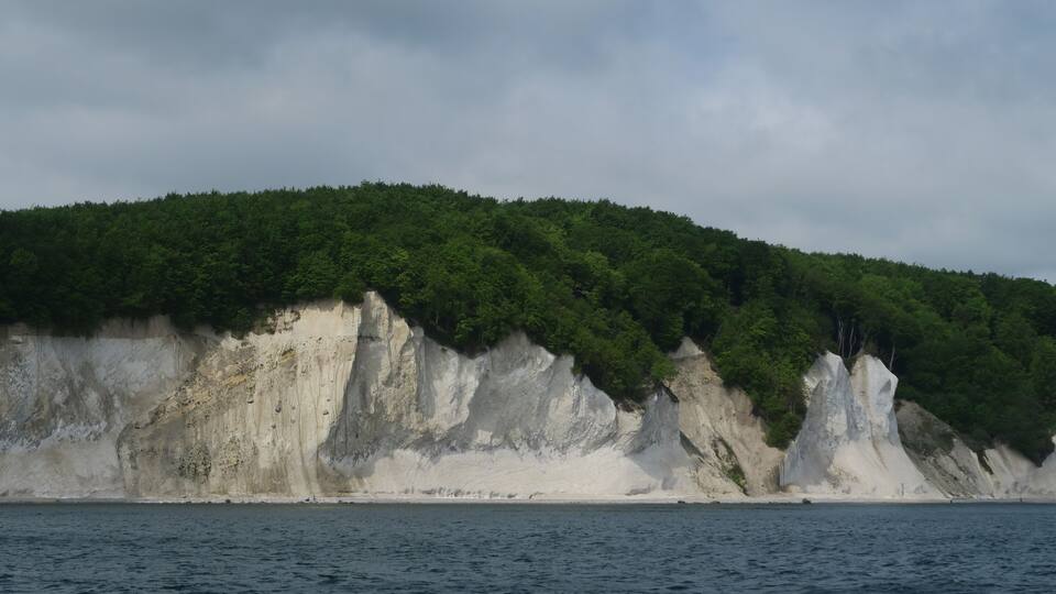 A coastal cliff with white rock formations and green vegetation.