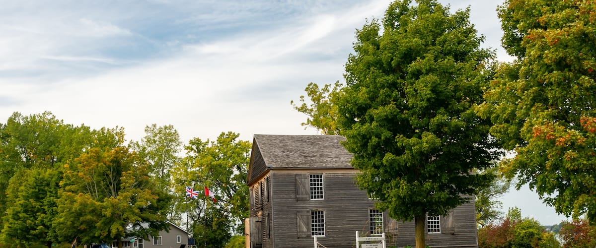 A historic wooden building with a sign, surrounded by trees and a clear sky.