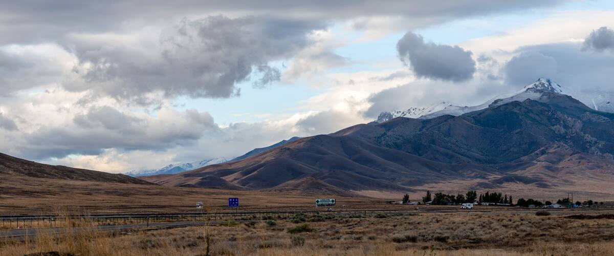 A highway with a mountainous landscape in the background, including a snow-capped peak.
