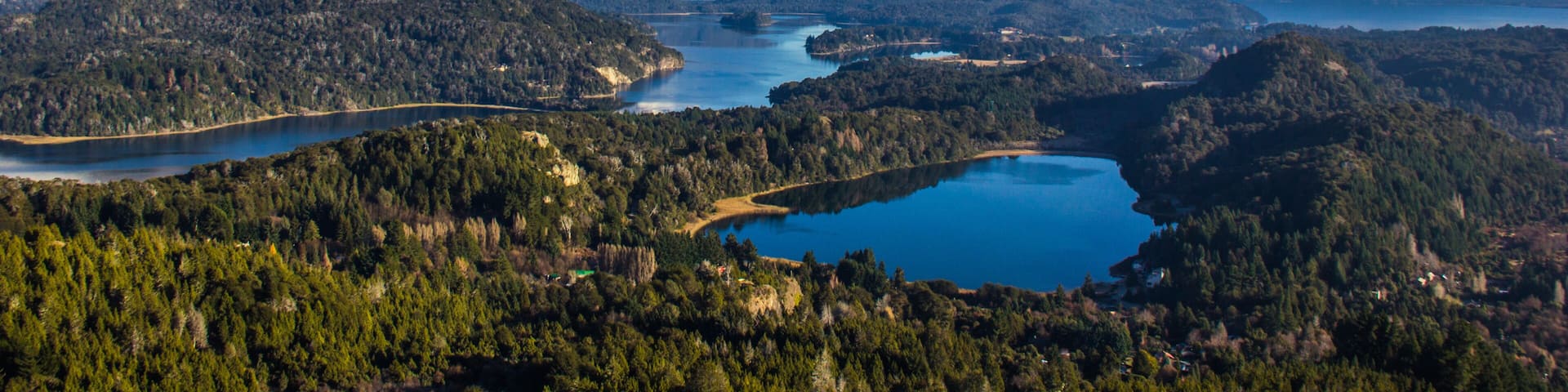 A mountainous landscape with a lake surrounded by dense forests and snow-capped peaks.