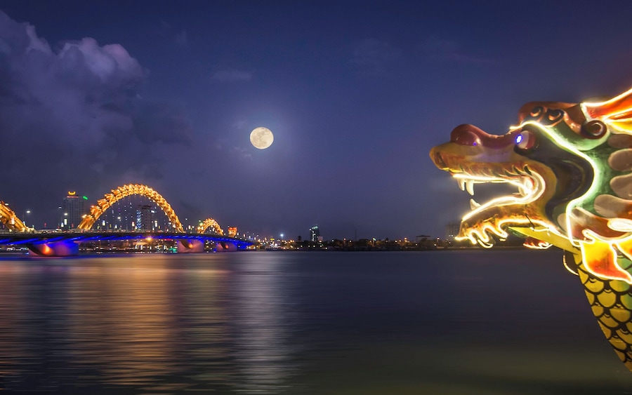 A bridge with illuminated arches and a dragon sculpture at night.