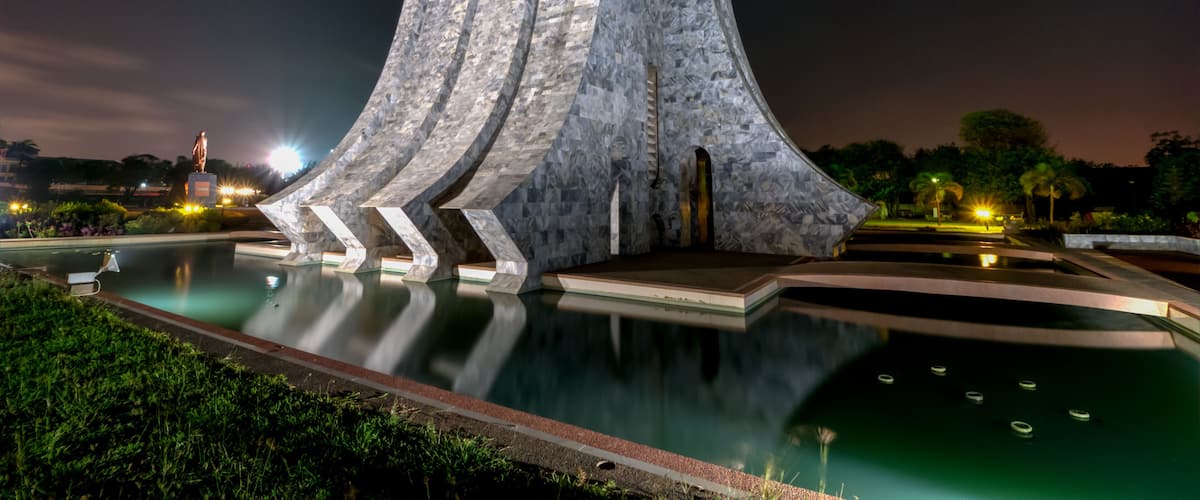 A modern sculpture with a reflective surface, a pool, and a statue in the background.