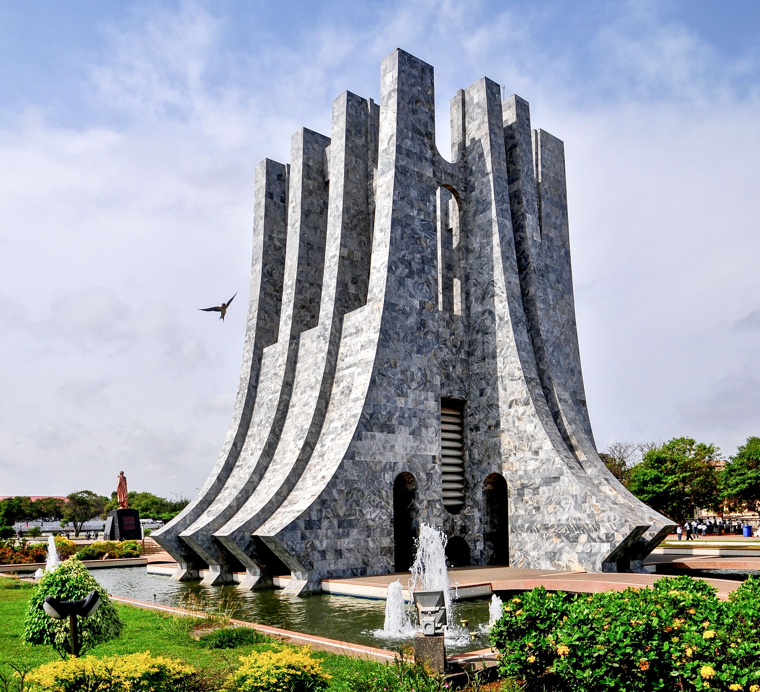 Una estructura arquitectónica moderna con varios elementos verticales y una fuente al frente.