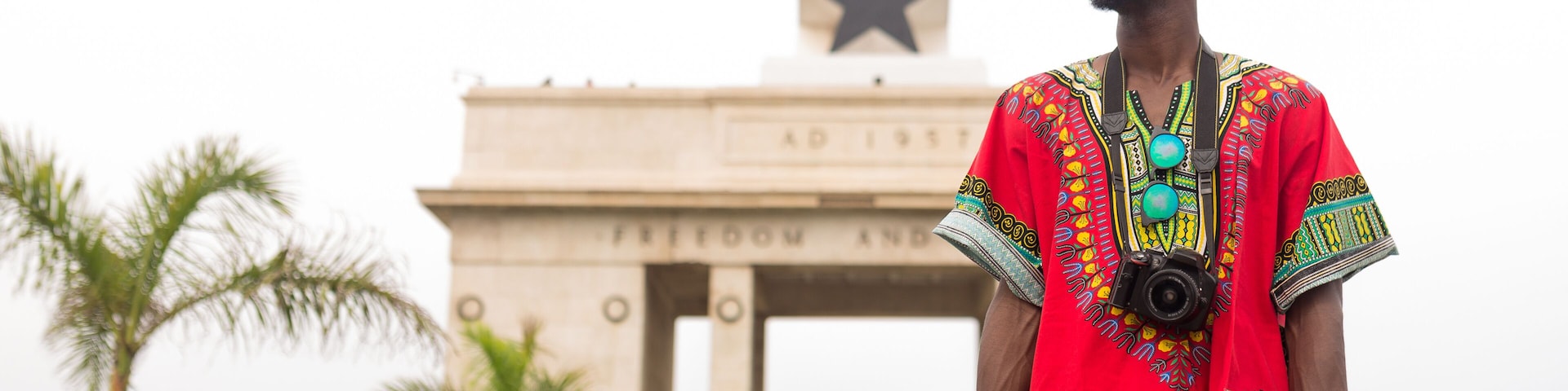 Una persona vestida con traje tradicional frente a un monumento con una estrella en la cima y la inscripción 'FREEDOM AND UNITY'.