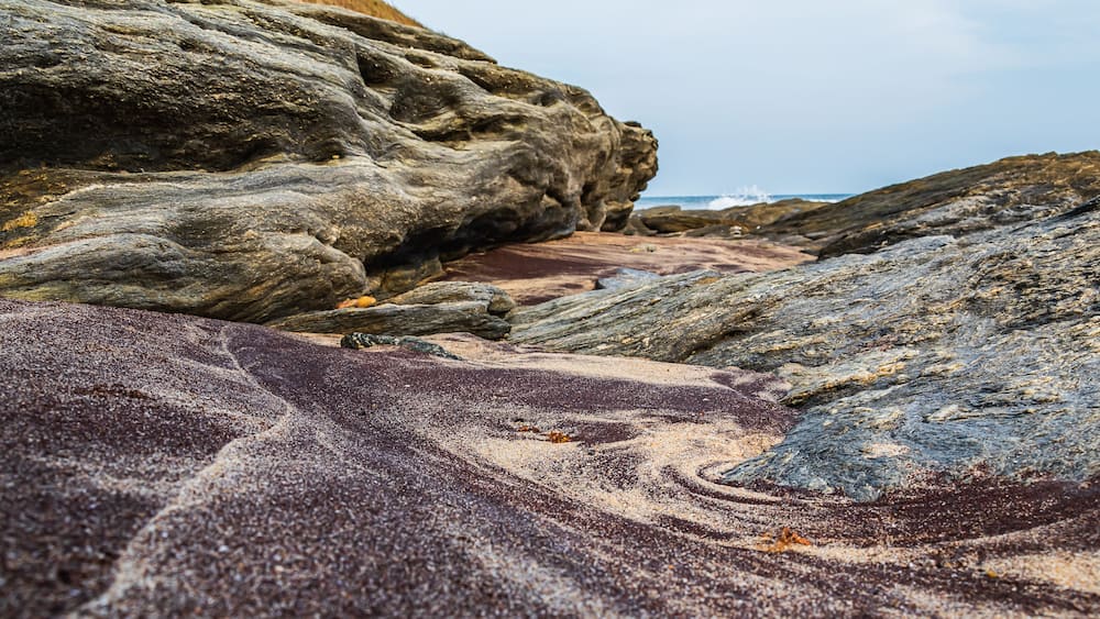 A rocky shoreline with a large boulder and a sandy area.
