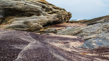 Uma costa rochosa com um grande rochedo e uma área de areia.