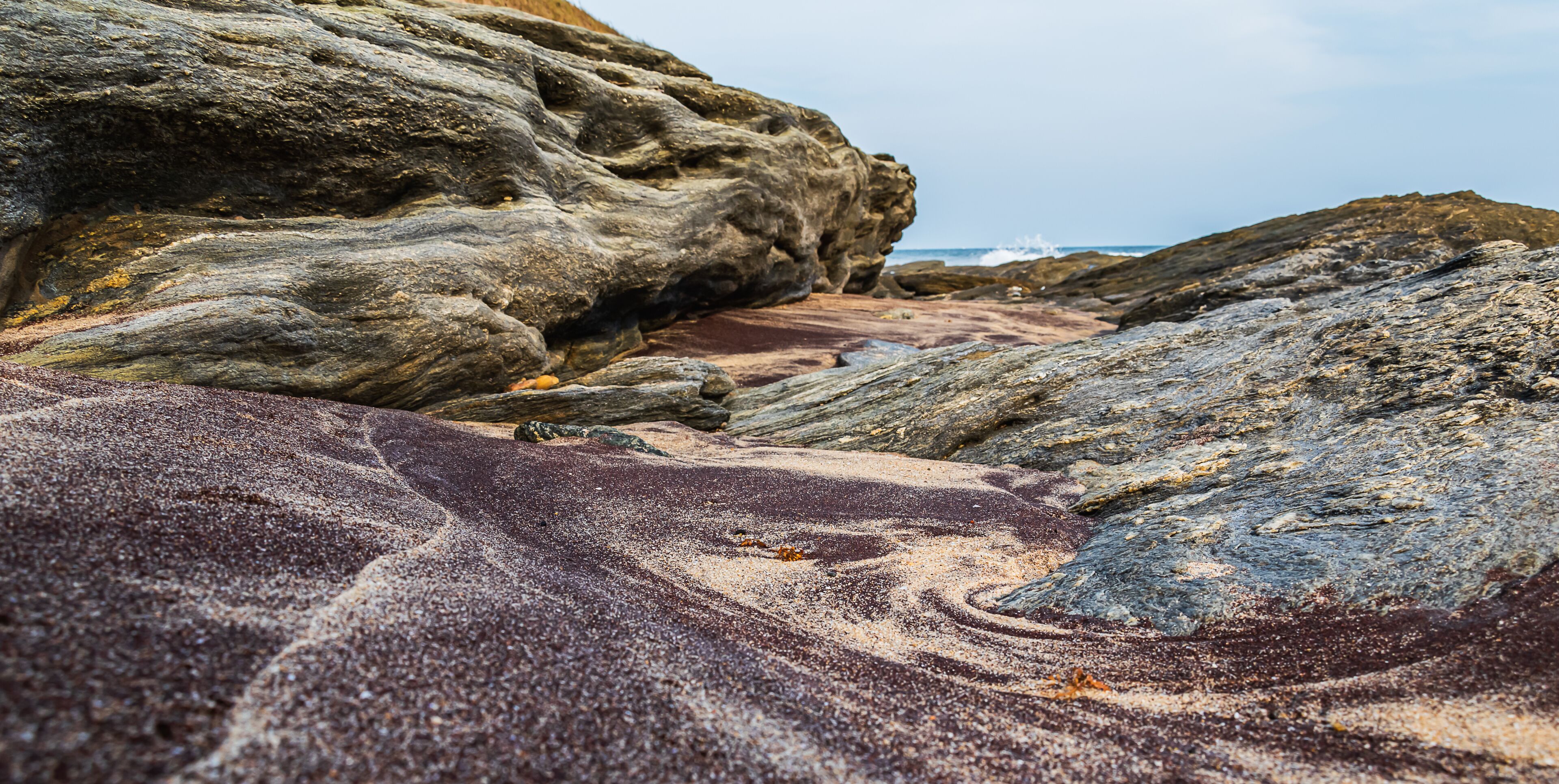 A rocky shoreline with a large boulder and a sandy area.