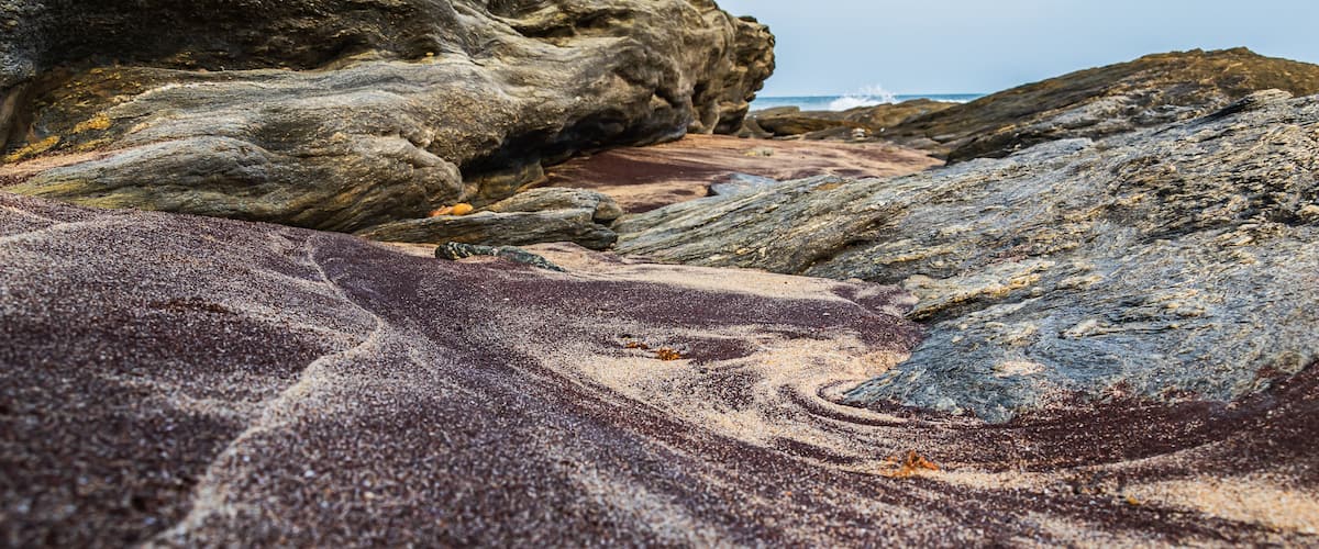 A rocky shoreline with a large boulder and a sandy area.