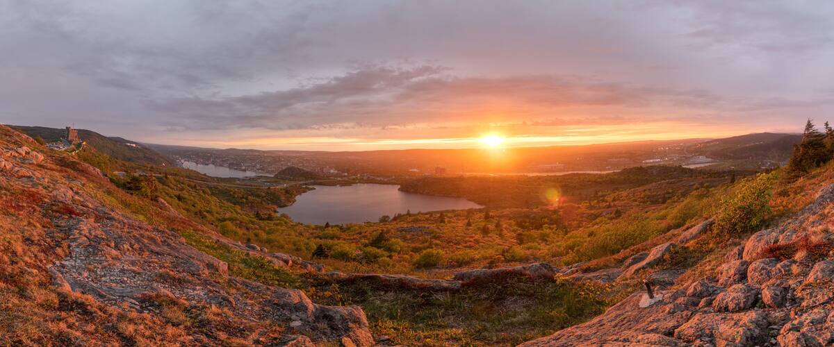 A sunset over a valley with a lake, surrounded by hills and sparse vegetation.