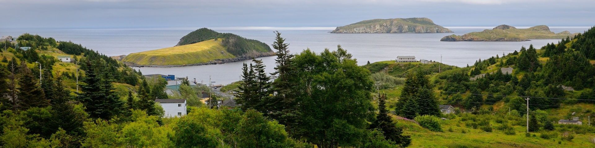 A curving road through a lush green landscape with distant islands and a cloudy sky.