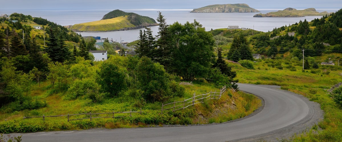 A curving road through a lush green landscape with distant islands and a cloudy sky.