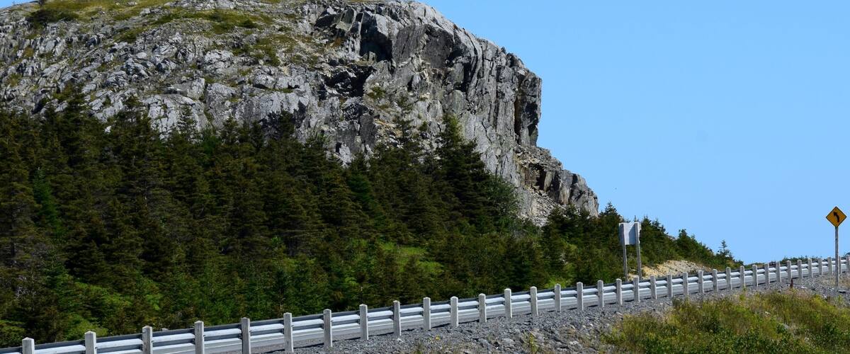 A rocky mountain with a guardrail and a warning sign.