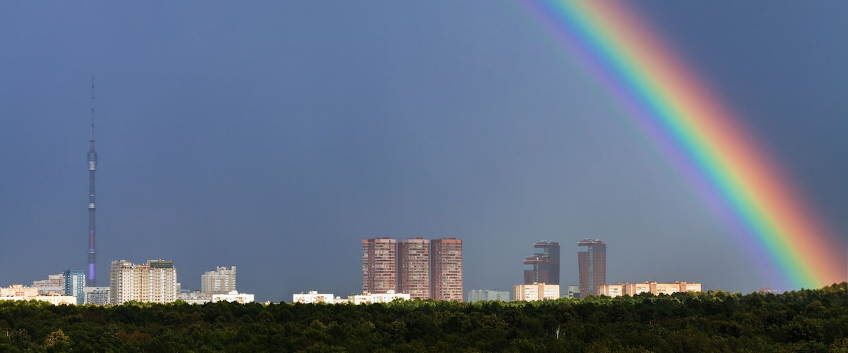 rainbow in dark blue sky over city with TV tower