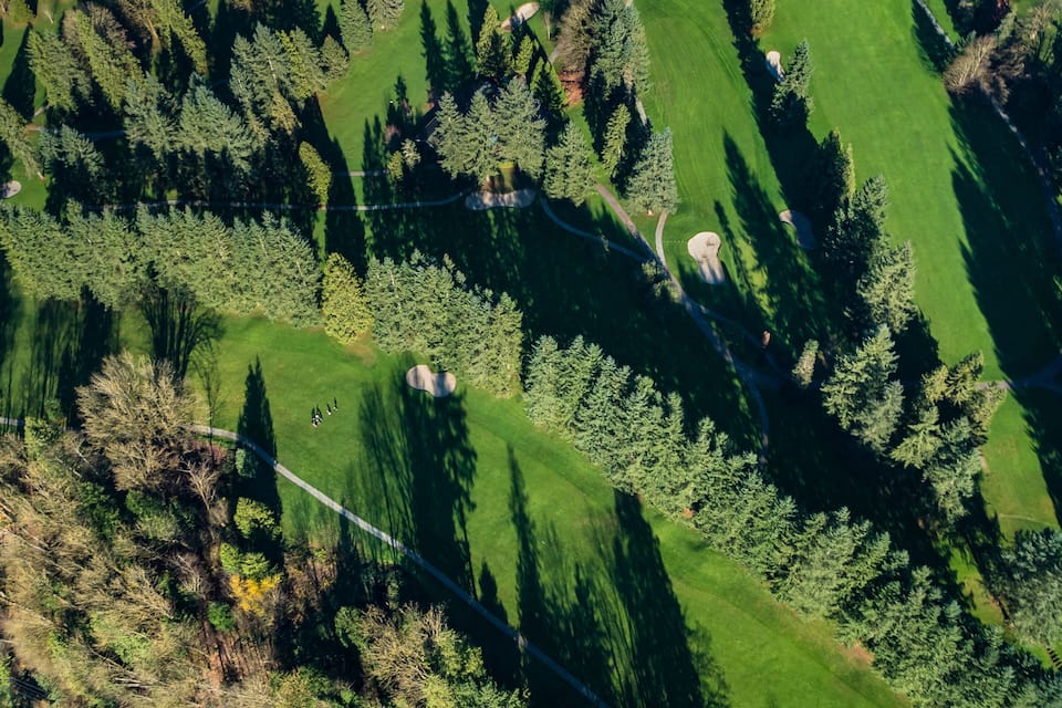 An aerial view of a golf course with neatly trimmed grass, sand bunkers, and a dense forest surrounding it.