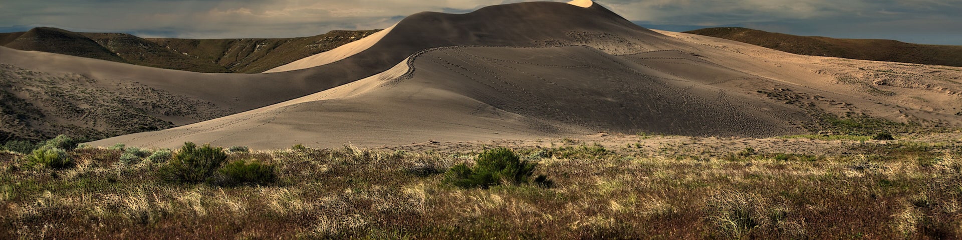 A desert landscape with sand dunes and a cloudy sky.