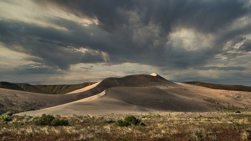 A desert landscape with sand dunes and a cloudy sky.