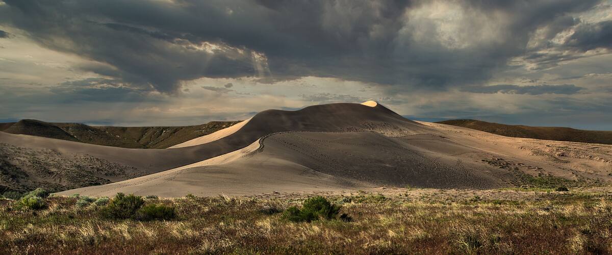 A desert landscape with sand dunes and a cloudy sky.