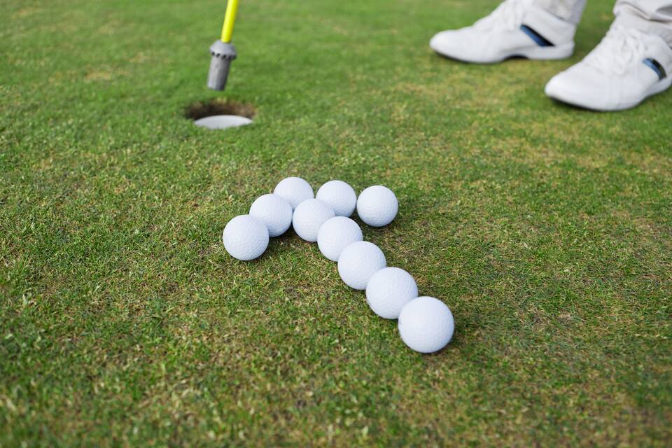 A golf course with a putting green, a hole, and a line of golf balls.