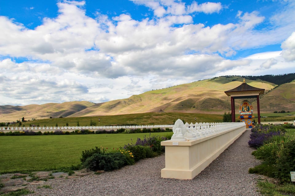 A pathway leading to a gazebo with a view of rolling hills and a cloudy sky.