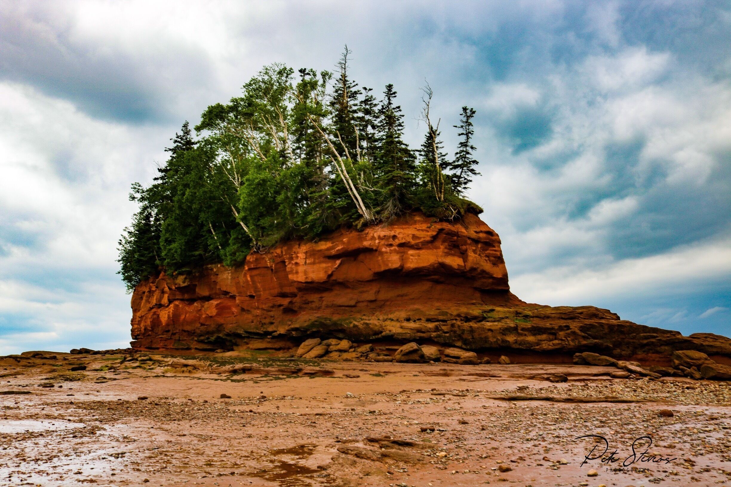 A rocky outcrop with trees on top and a cloudy sky.