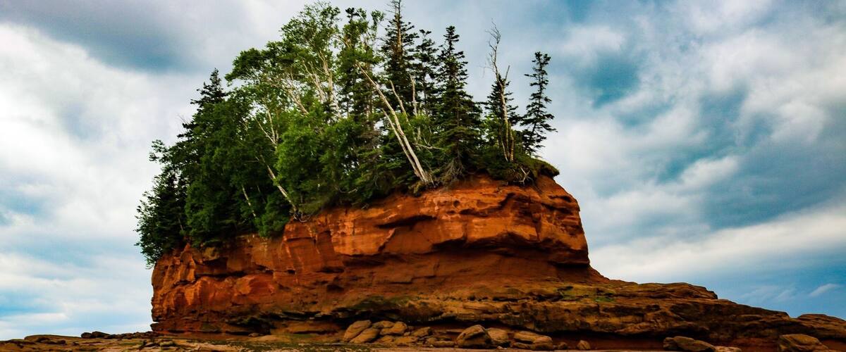 A rocky outcrop with trees on top and a cloudy sky.
