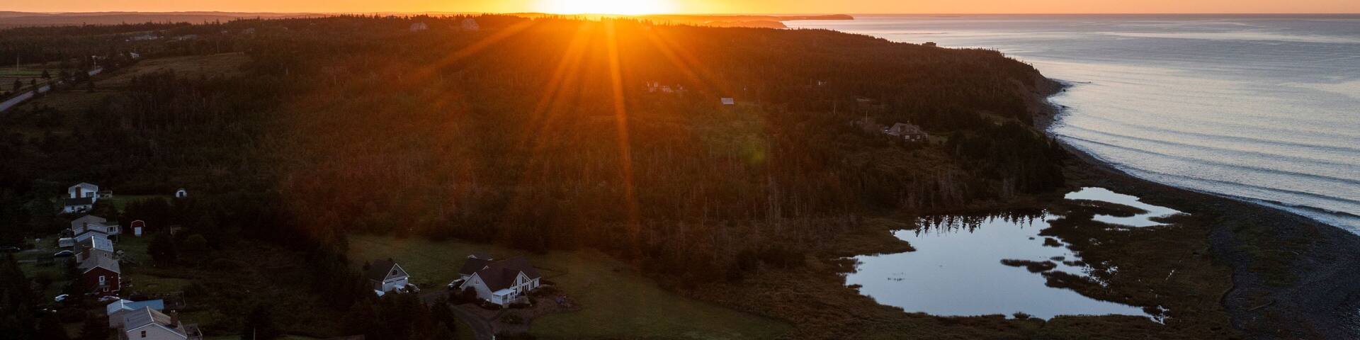 Aerial view of beautiful sunset over tranquil coastline with forest and homes, Lawrencetown, Canada.