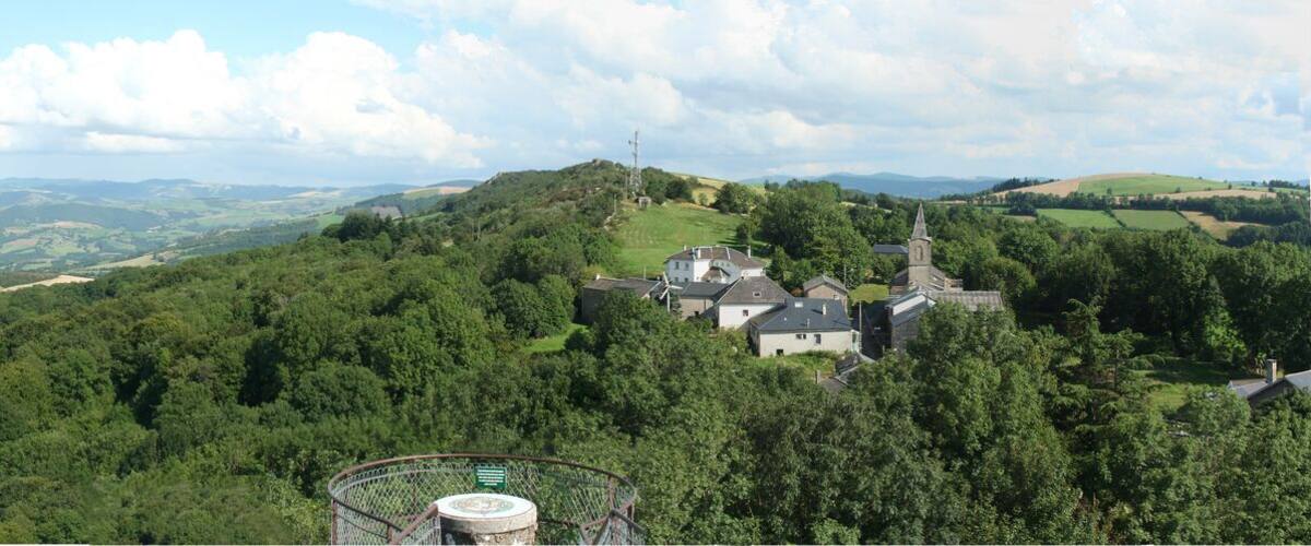 A panoramic view of a lush valley with rolling hills, a church on a hilltop, and a distant power line tower.