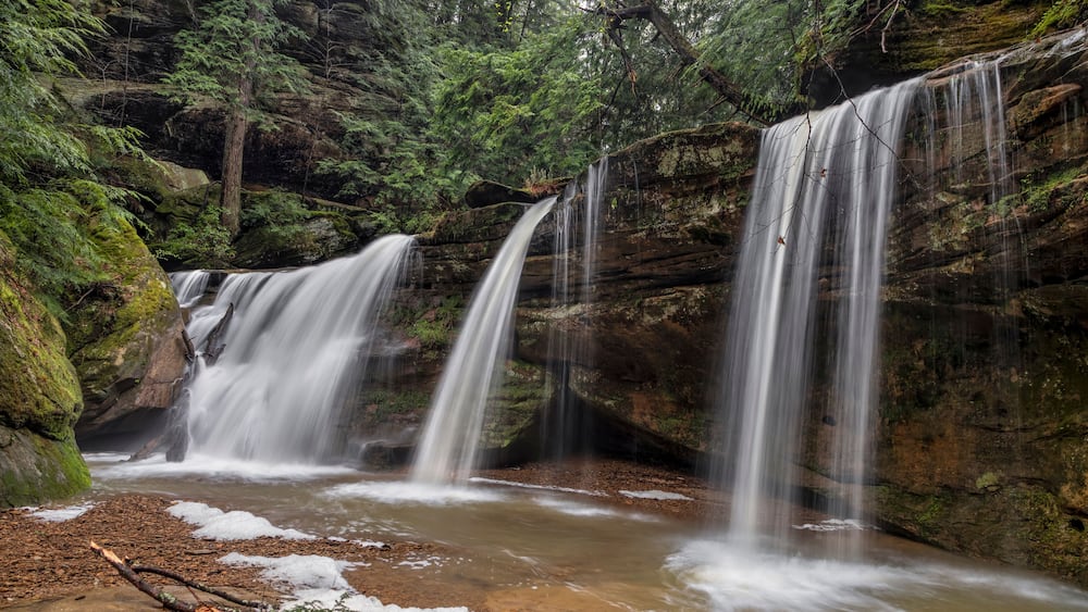 A waterfall cascading over moss-covered rocks in a forested area.