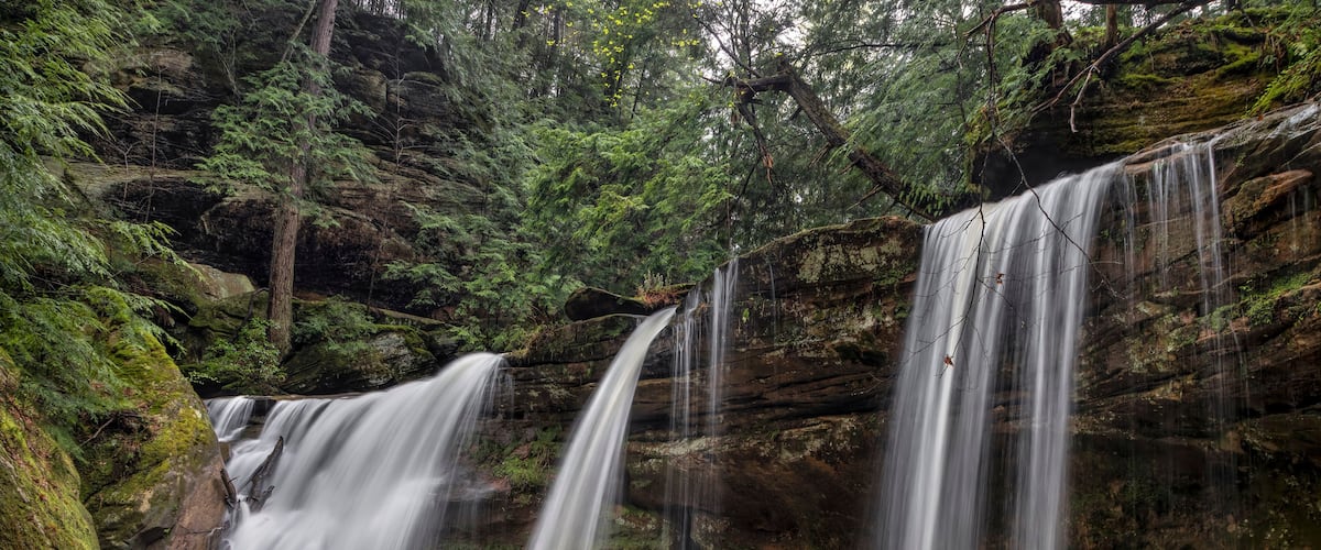 A waterfall cascading over moss-covered rocks in a forested area.