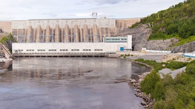 A hydroelectric dam with a river flowing through it, surrounded by rocky terrain and greenery.