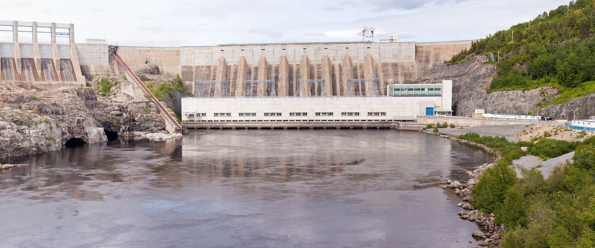 A hydroelectric dam with a river flowing through it, surrounded by rocky terrain and greenery.